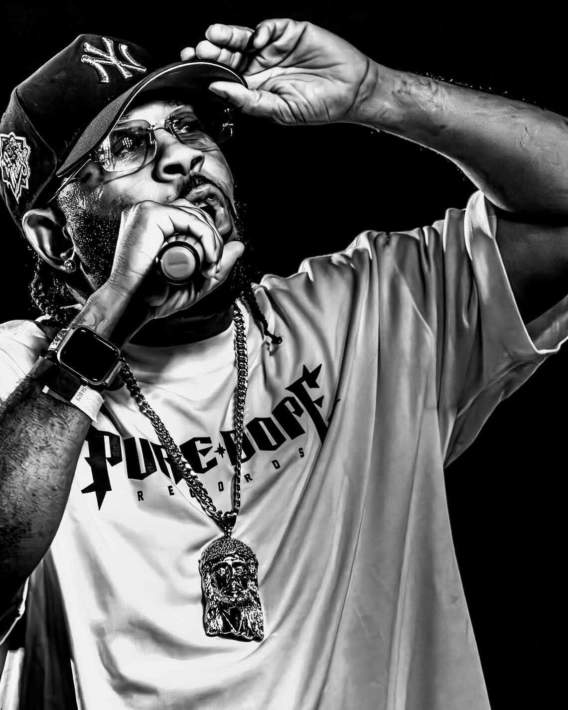 P.GUTTER on stage, mic in hand, adjusting his Yankees cap, in a Pure Dope Records tee